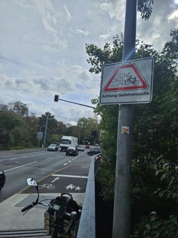 Am Ende der Maxbrücke hängt rechts ein Schild neben dem Radweg: "Achtung Gefahrenstelle". Der Verkehr voraus ist unübersichtlich. Ein LKW will gerade links abbiegen und dabei den Radweg kreuzen.