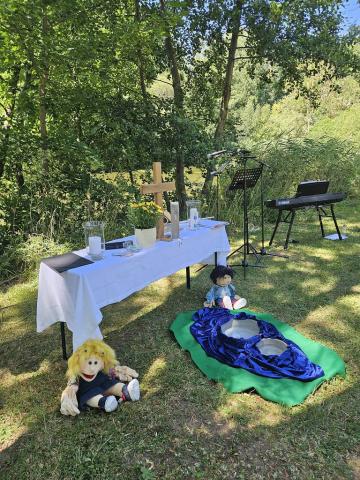 Ein Altar im Freien am See, zwei Stoff-Handpuppen sitzen davor.