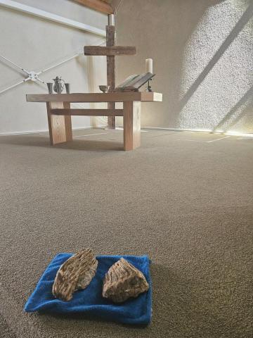 Zwei Mammutzähne liegen auf einem blauen Tuch. Im Hintergrund der schlicht gehaltene Altar der Doopsgezinde Gemeente Ouddorp mit einem großen Holzkreuz dahinter. Von rechts oben fällt Licht auf die Szene.