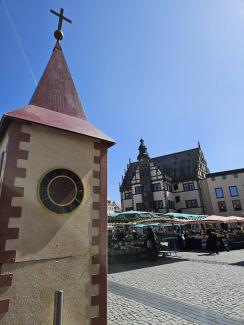 Der Turm der Wagenkirche. Im Hintergrund sieht man Marktstände und das Schweinfurter Rathaus. Alles unter strahlend blauem Himmel.