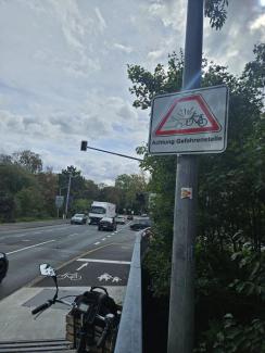 Am Ende der Maxbrücke hängt rechts ein Schild neben dem Radweg: "Achtung Gefahrenstelle". Der Verkehr voraus ist unübersichtlich. Ein LKW will gerade links abbiegen und dabei den Radweg kreuzen.